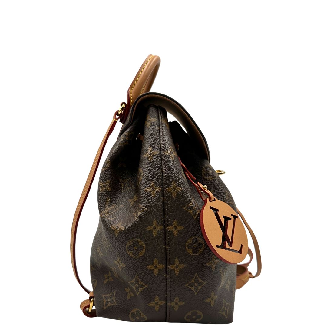 Laterale di uno zaino Montsouris NM in canvas marrone monogram con finiture in vacchetta naturale e parti metalliche dorate, munito di un manico sulla parte superiore e due bretelle in vacchetta regolabili. Completo di corredo e charm decorativo.
