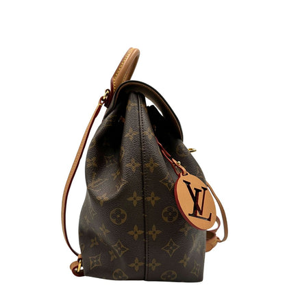 Laterale di uno zaino Montsouris NM in canvas marrone monogram con finiture in vacchetta naturale e parti metalliche dorate, munito di un manico sulla parte superiore e due bretelle in vacchetta regolabili. Completo di corredo e charm decorativo.