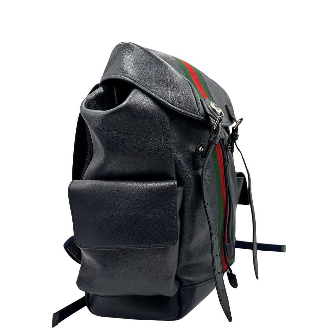 Laterale sinistro di uno zaino Gucci in canvas pelle blu notte, con parti metalliche argentate. Iconica striscia Web in verde/rosso sul front, con cinghie regolabili e tasche laterali. Completo di dustbag.