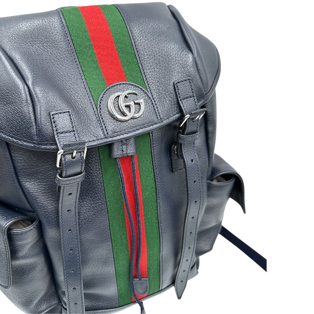 Vista superiore di uno zaino Gucci in canvas pelle blu notte, con parti metalliche argentate. Iconica striscia Web in verde/rosso sul front, con cinghie regolabili e tasche laterali. Completo di dustbag.