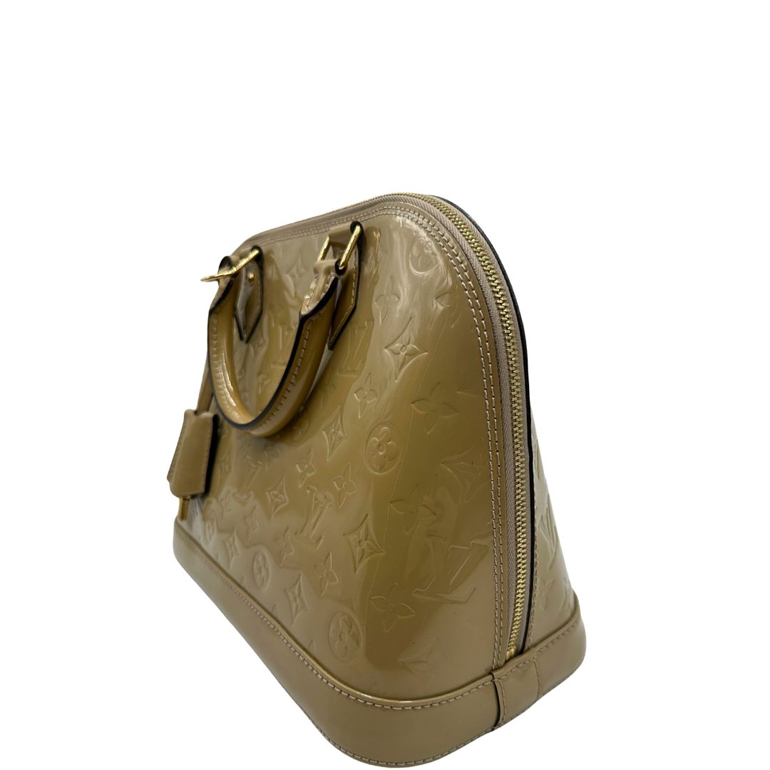 Laterale destro di una borsa Alma PM Louis Vuitton in pelle Vernis color noisette con parti metalliche dorate e doppi manici stondati; da portare a mano. Completa di lucchetto e chiavi.