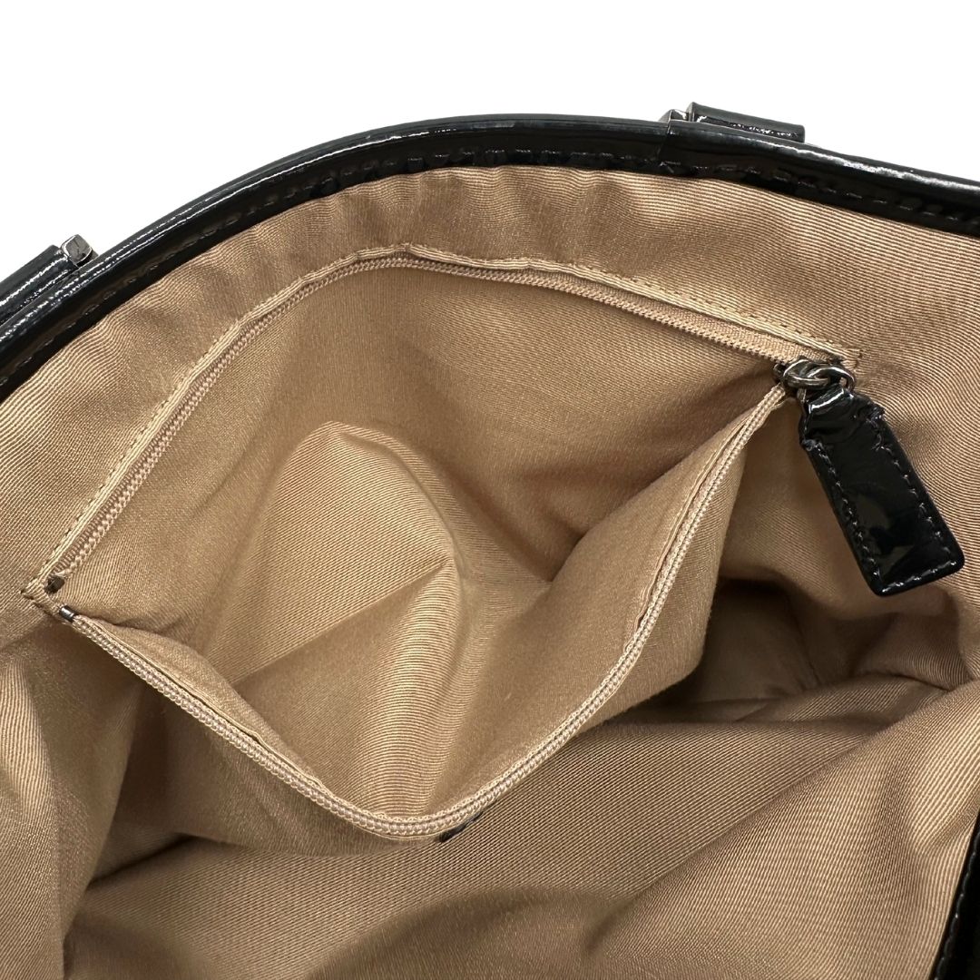 Interno di una borsa Burberry in canvas beige tartan con finiture in pelle nera lucida e parti metalliche effetto renio. Munita di doppi manici stondati. Completa di dustbag.