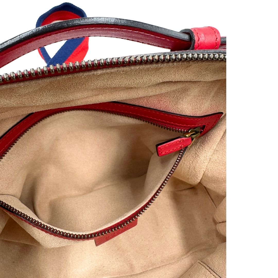 Interno di una borsa Gucci Marmont in pelle matelassè rossa e parti metalliche dorate; munita di un manico superiore e di una tracolla in tessuto web blu/bianco/rosso, regolabile ed amovibile. Indossabile a mano o a tracolla. Completa di dustbag.