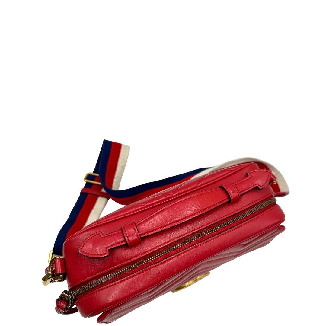 Vista superiore di una borsa Gucci Marmont in pelle matelassè rossa e parti metalliche dorate; munita di un manico superiore e di una tracolla in tessuto web blu/bianco/rosso, regolabile ed amovibile. Indossabile a mano o a tracolla. Completa di dustbag.