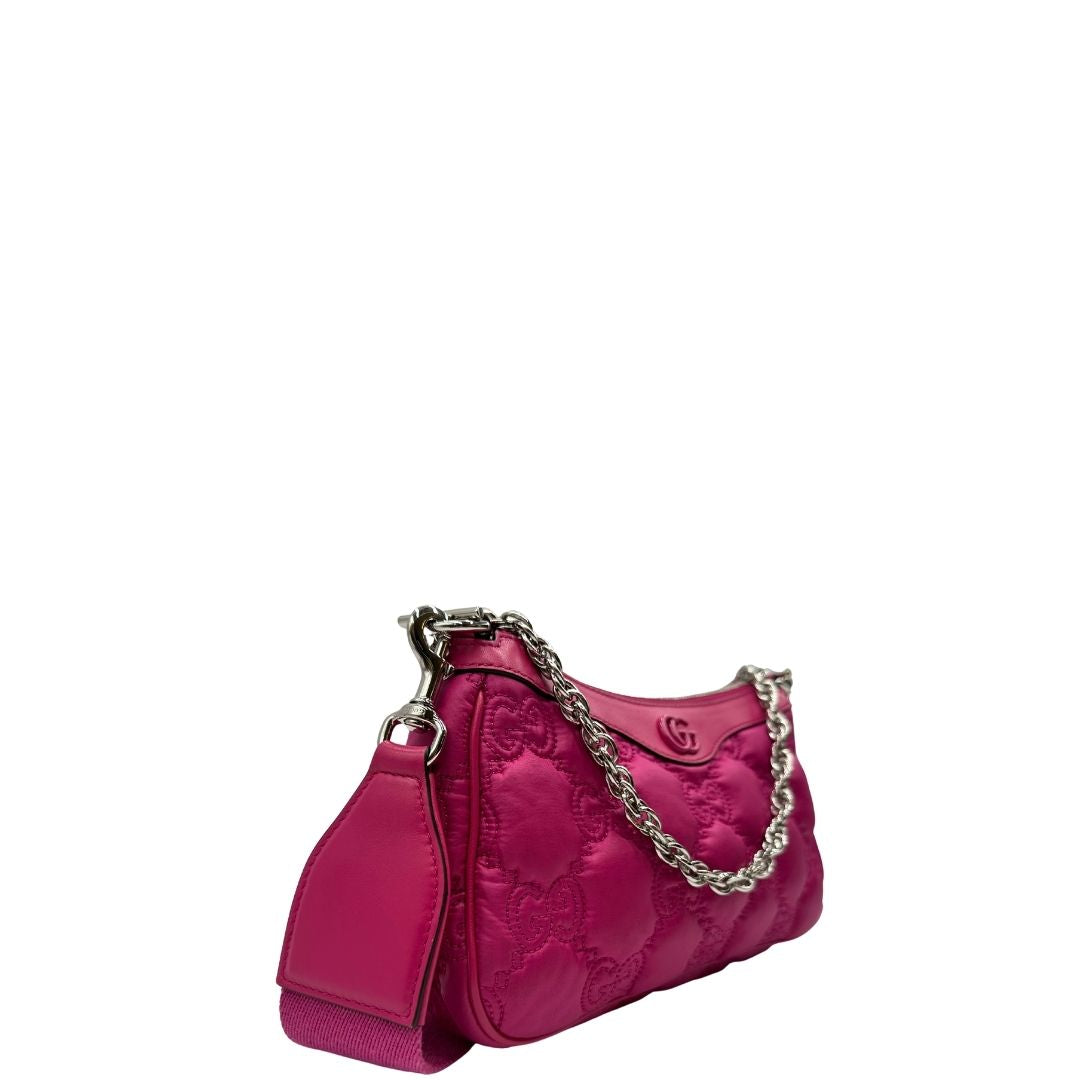 Laterale sinistro di una borsa Gucci in nylon trapuntato matelassé fucsia con trama GG, finiture in pelle tono su tono, manico singolo in catena e tracolla in tessuto regolabile ed amovibile. Rifinita con parti metalliche argentate. Completa di dustbag.