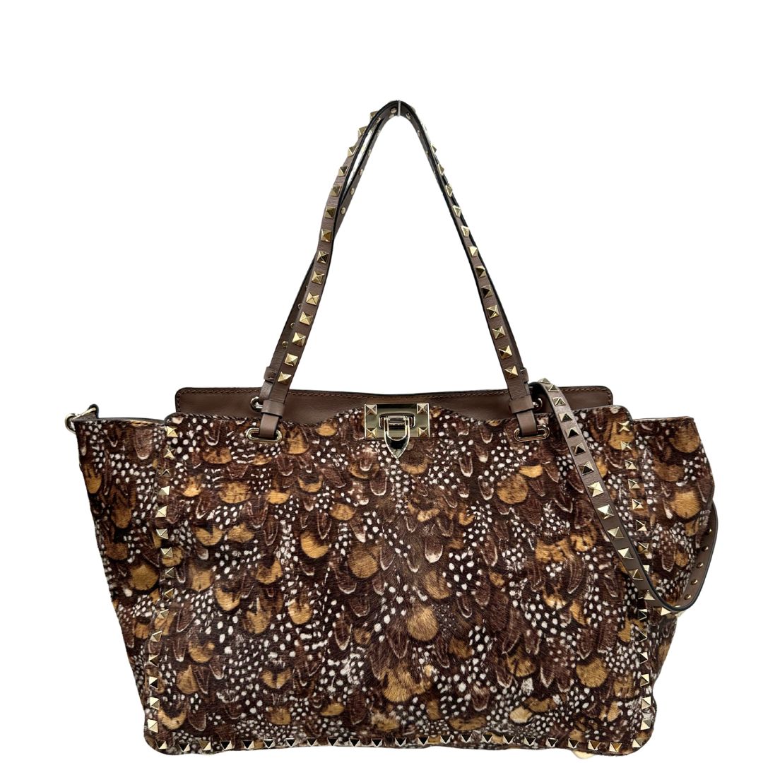 Front di una Borsa Prada effetto cavallino stampato con piume multicolore e finiture in pelle marrone, con parti metalliche dorate; impreziosita da borchie piramidali e munita di doppi manici e tracolla amovibile. Completa di dustbag. Originale, usata, di lusso, in ottime condizioni.