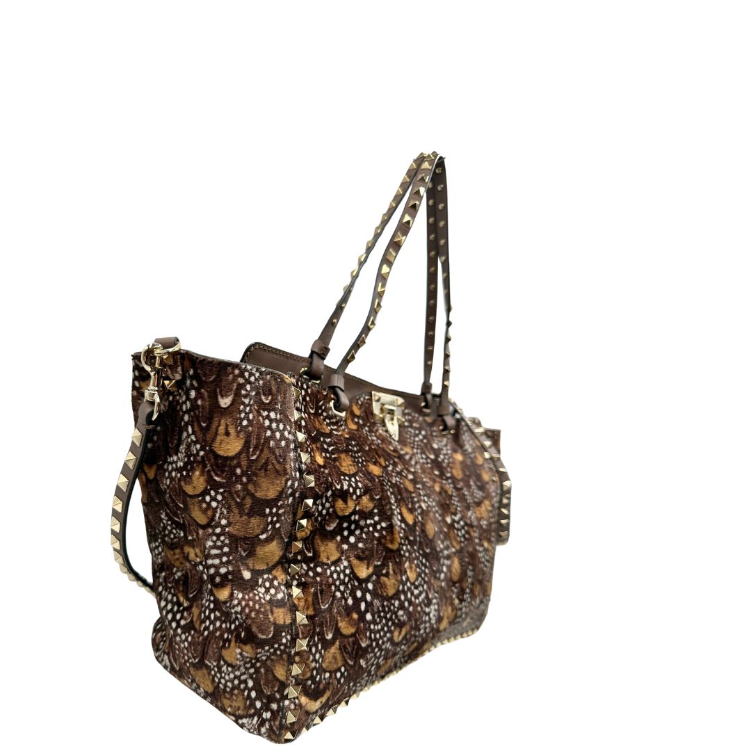Lato destro di una Borsa Prada effetto cavallino stampato con piume multicolore e finiture in pelle marrone, con parti metalliche dorate; impreziosita da borchie piramidali e munita di doppi manici e tracolla amovibile. Completa di dustbag. Originale, usata, di lusso, in ottime condizioni.
