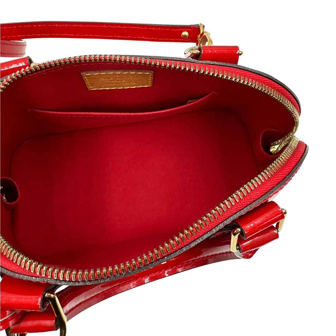Interno di una borsa Louis Vuitton Alma BB in pelle vernis rossa con trama monogram empreinte e parti metalliche dorate. Munita di doppi manici stondati e tracolla amovibile, dotata di clochette porta chiavi. Completa di scatola, dustbag, lucchetto e chiavi.
