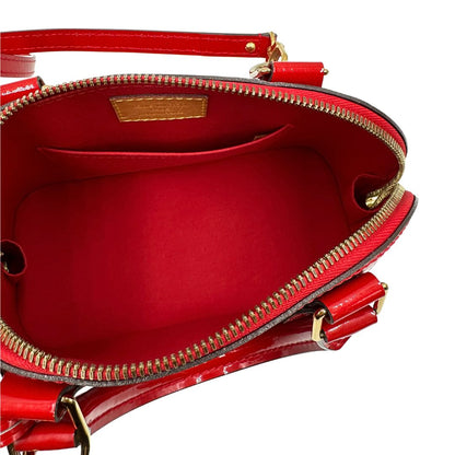 Interno di una borsa Louis Vuitton Alma BB in pelle vernis rossa con trama monogram empreinte e parti metalliche dorate. Munita di doppi manici stondati e tracolla amovibile, dotata di clochette porta chiavi. Completa di scatola, dustbag, lucchetto e chiavi.