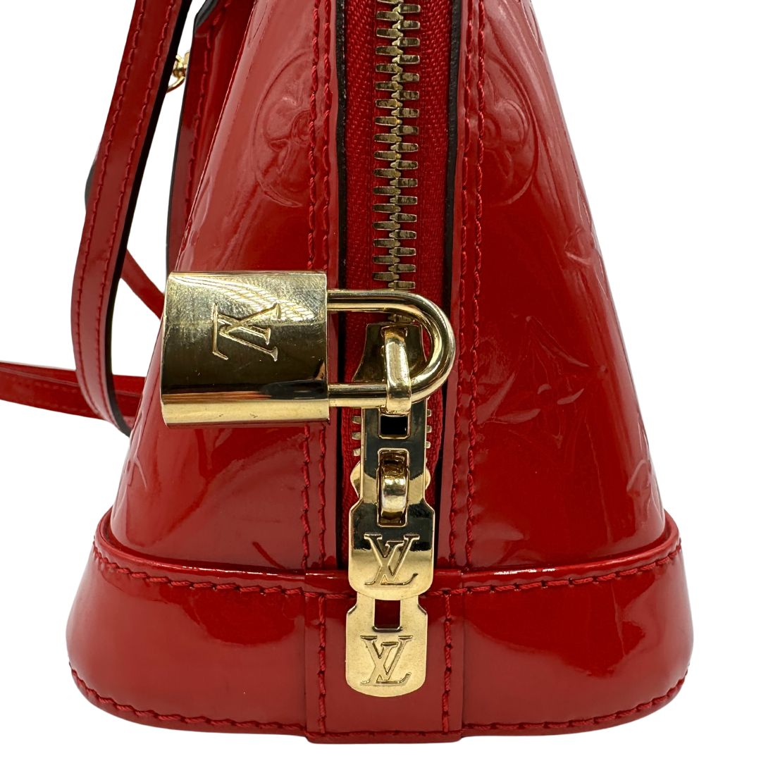 Lucchetto di una borsa Louis Vuitton Alma BB in pelle vernis rossa con trama monogram empreinte e parti metalliche dorate. Munita di doppi manici stondati e tracolla amovibile, dotata di clochette porta chiavi. Completa di scatola, dustbag e chiavi.