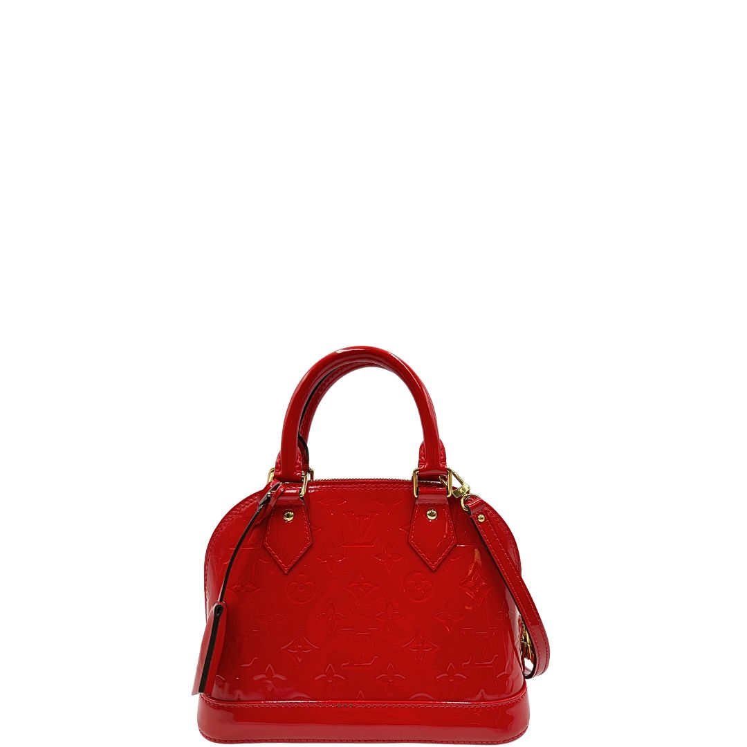 Front di una borsa Louis Vuitton Alma BB in pelle vernis rossa con trama monogram empreinte e parti metalliche dorate. Munita di doppi manici stondati e tracolla amovibile, dotata di clochette porta chiavi. Completa di scatola, dustbag, lucchetto e chiavi.