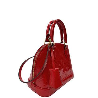 Laterale sinistro di una borsa Louis Vuitton Alma BB in pelle vernis rossa con trama monogram empreinte e parti metalliche dorate. Munita di doppi manici stondati e tracolla amovibile, dotata di clochette porta chiavi. Completa di scatola, dustbag, lucchetto e chiavi.