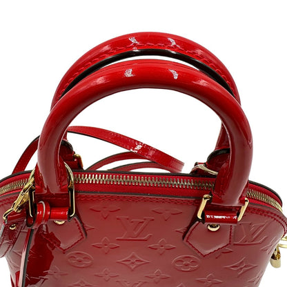 Manici di una borsa Louis Vuitton Alma BB in pelle vernis rossa con trama monogram empreinte e parti metalliche dorate. Munita di doppi manici stondati e tracolla amovibile, dotata di clochette porta chiavi. Completa di scatola, dustbag, lucchetto e chiavi.