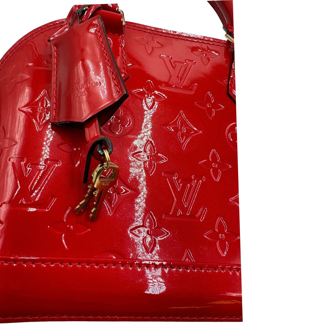 Chiavi e clochette di una borsa Louis Vuitton Alma BB in pelle vernis rossa con trama monogram empreinte e parti metalliche dorate. Munita di doppi manici stondati e tracolla amovibile. Completa di scatola, dustbag e lucchetto.