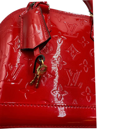 Chiavi e clochette di una borsa Louis Vuitton Alma BB in pelle vernis rossa con trama monogram empreinte e parti metalliche dorate. Munita di doppi manici stondati e tracolla amovibile. Completa di scatola, dustbag e lucchetto.
