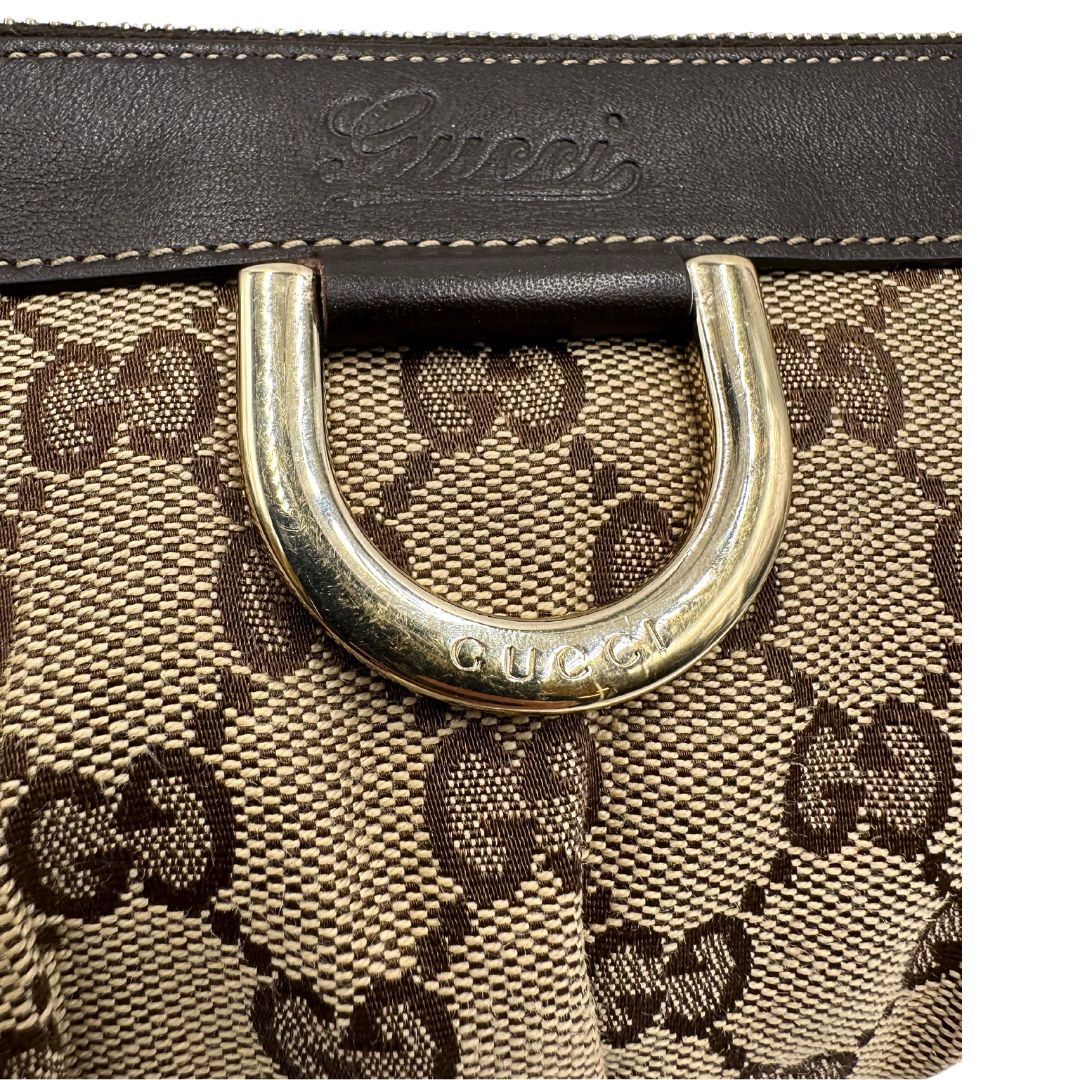 Dettaglio metallico di una pochette Gucci in tessuto Gucci in tessuto GG beige con finiture in pelle marrone e parti metalliche dorate; munita di un polsino, da portare a mano. Completa di dustbag.