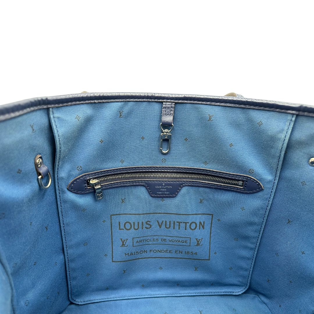 Interno di una borsa Louis Vuitton Neverfull MM in canvas base tie-dye nelle tonalità del blu e bianco, con finiture in pelle blu navy. Da un lato ha stampa Monogram Giant, dall'altra Monogram. Parti metalliche argentate; munita di doppi manici e dustbag, indossabile a spalla.