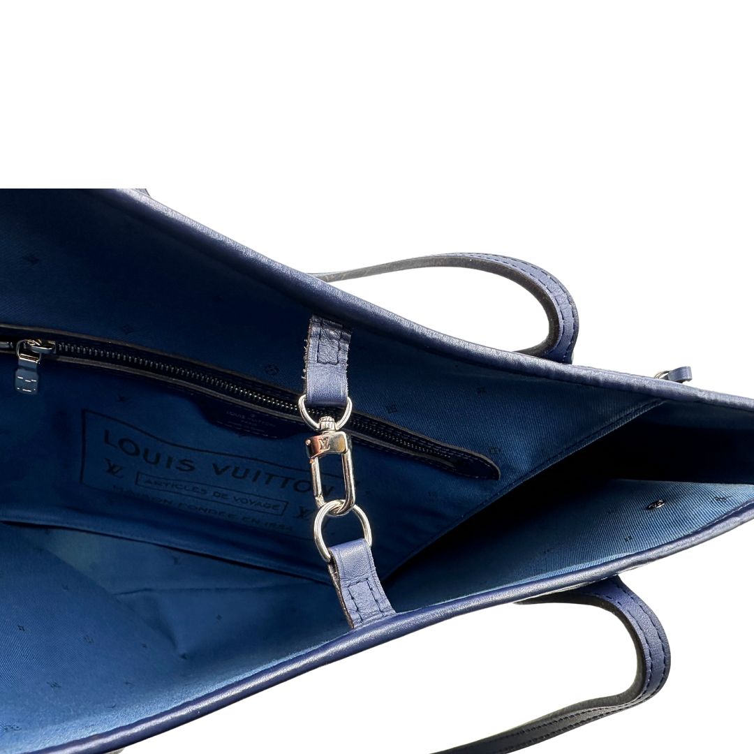 Chiusura di una borsa Louis Vuitton Neverfull MM in canvas base tie-dye nelle tonalità del blu e bianco, con finiture in pelle blu navy. Da un lato ha stampa Monogram Giant, dall'altra Monogram. Parti metalliche argentate; munita di doppi manici e dustbag, indossabile a spalla.