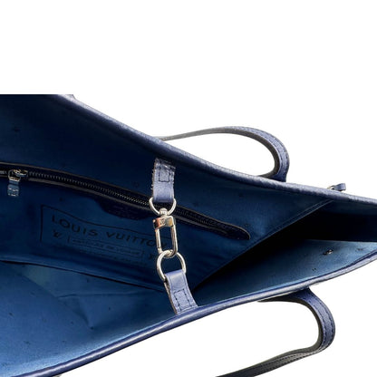 Chiusura di una borsa Louis Vuitton Neverfull MM in canvas base tie-dye nelle tonalità del blu e bianco, con finiture in pelle blu navy. Da un lato ha stampa Monogram Giant, dall'altra Monogram. Parti metalliche argentate; munita di doppi manici e dustbag, indossabile a spalla.