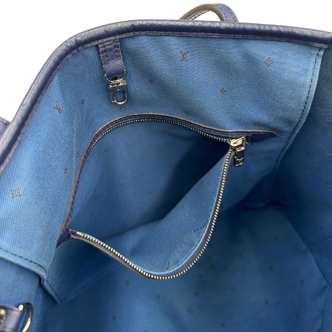 Interno di una borsa Louis Vuitton Neverfull MM in canvas base tie-dye nelle tonalità del blu e bianco, con finiture in pelle blu navy. Da un lato ha stampa Monogram Giant, dall'altra Monogram. Parti metalliche argentate; munita di doppi manici e dustbag, indossabile a spalla.