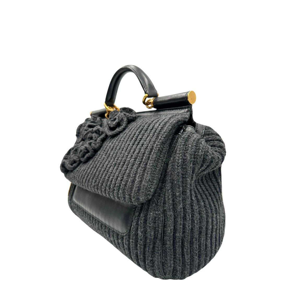 Lato sinistro di una Borsa D&G Miss Sicily in lana grigia con parti metalliche dorate e finiture in pelle nera e dettagli fiori ; munita di un manico singolo stondato e ciondolo logato. completa di dustbag e card d'autenticità. Originale, usata, di lusso, in ottime condizione.