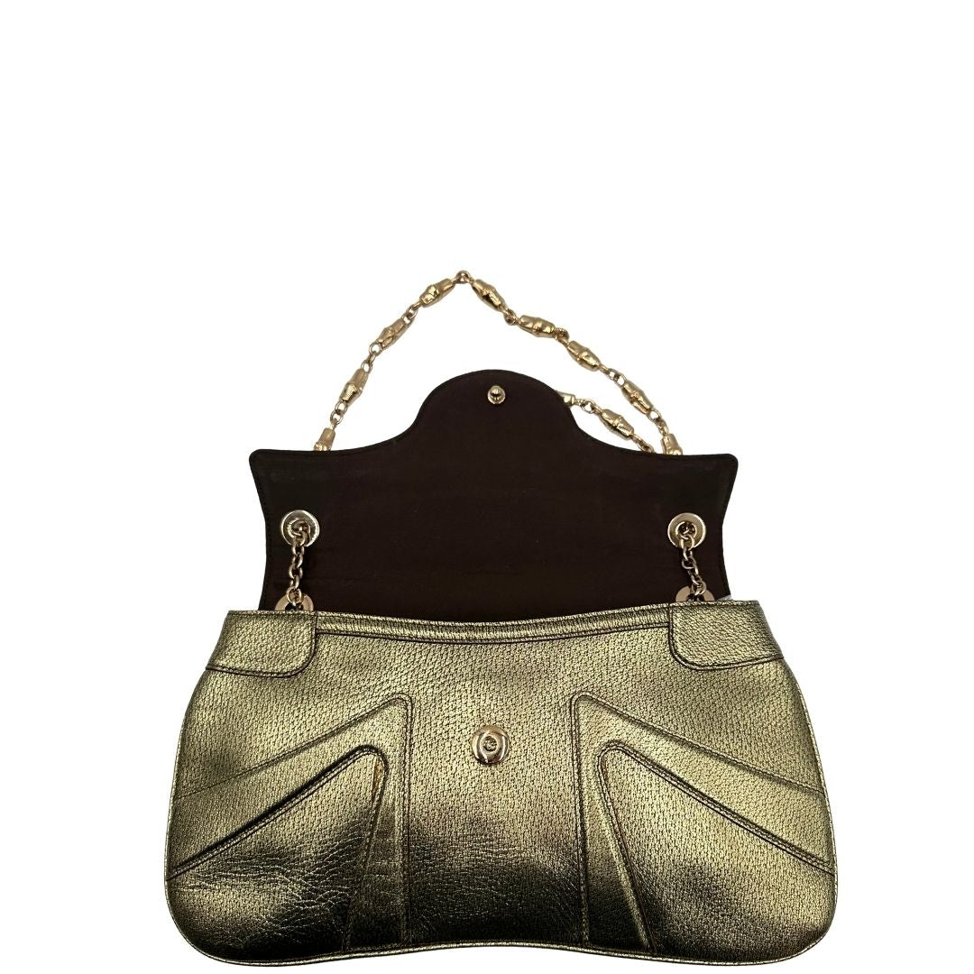 Apertura di una borsa Gucci in pelle color oro anticato, dettaglio gioiello circolare sulla patta di chiusura composto da due teste di drago contrapposte, smaltate e decorate con micro strass, parti metalliche dorate; munita di doppi manici in catena a maglie. Indossabile a spalla.