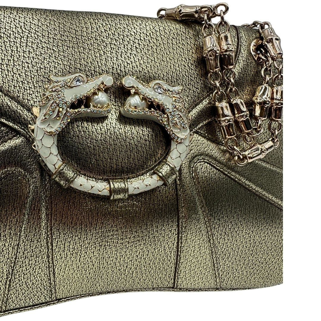 Dettaglio decorativo di una borsa Gucci in pelle color oro anticato, dettaglio gioiello circolare sulla patta di chiusura composto da due teste di drago contrapposte, smaltate e decorate con micro strass, parti metalliche dorate; munita di doppi manici in catena a maglie. Indossabile a spalla.