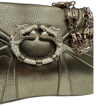 Dettaglio decorativo di una borsa Gucci in pelle color oro anticato, dettaglio gioiello circolare sulla patta di chiusura composto da due teste di drago contrapposte, smaltate e decorate con micro strass, parti metalliche dorate; munita di doppi manici in catena a maglie. Indossabile a spalla.