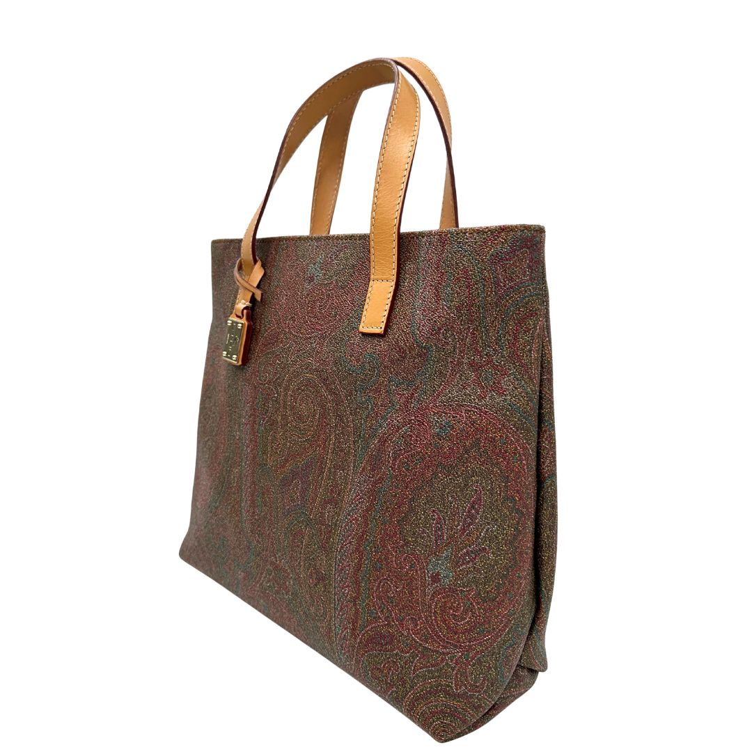Laterale destro di una borsa Etro in canvas trama paisley in varie tonalità calde e parti in pelle beige, dettagli metallici dorati, munita di doppi manici. Indossabile a mano. Completa di dustbag e charm decorativo amovibile.