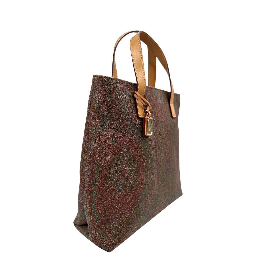 Laterale sinistro di una borsa Etro in canvas trama paisley in varie tonalità calde e parti in pelle beige, dettagli metallici dorati, munita di doppi manici. Indossabile a mano. Completa di dustbag e charm decorativo amovibile.