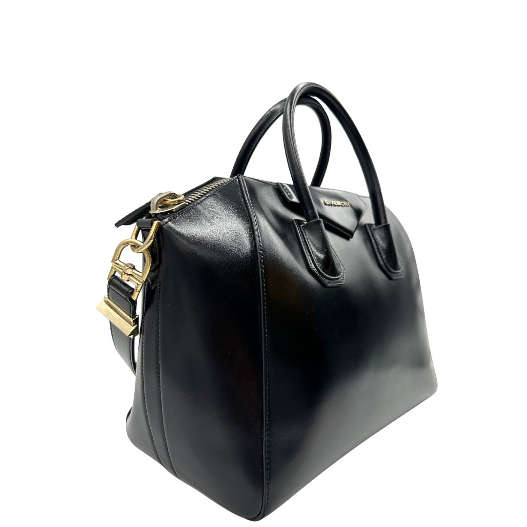 Laterale sinistro di una borsa Givenchy Antigona in pelle nera munita di doppi manici stondati, parti metalliche dorate e una tracolla non amovibile e non regolabile.