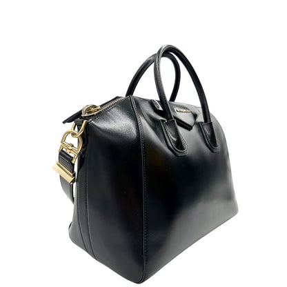 Laterale sinistro di una borsa Givenchy Antigona in pelle nera munita di doppi manici stondati, parti metalliche dorate e una tracolla non amovibile e non regolabile.