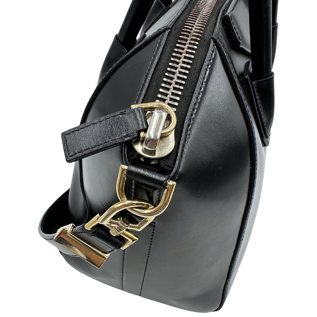 Dettagli metallici di una borsa Givenchy Antigona in pelle nera munita di doppi manici stondati, parti metalliche dorate e una tracolla non amovibile e non regolabile.