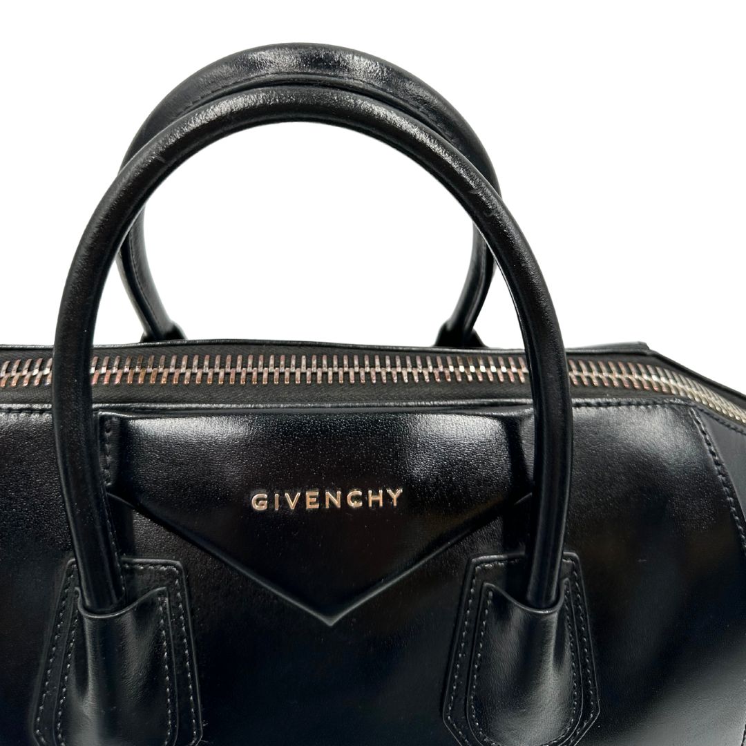 Manici di una borsa Givenchy Antigona in pelle nera munita di doppi manici stondati, parti metalliche dorate e una tracolla non amovibile e non regolabile.