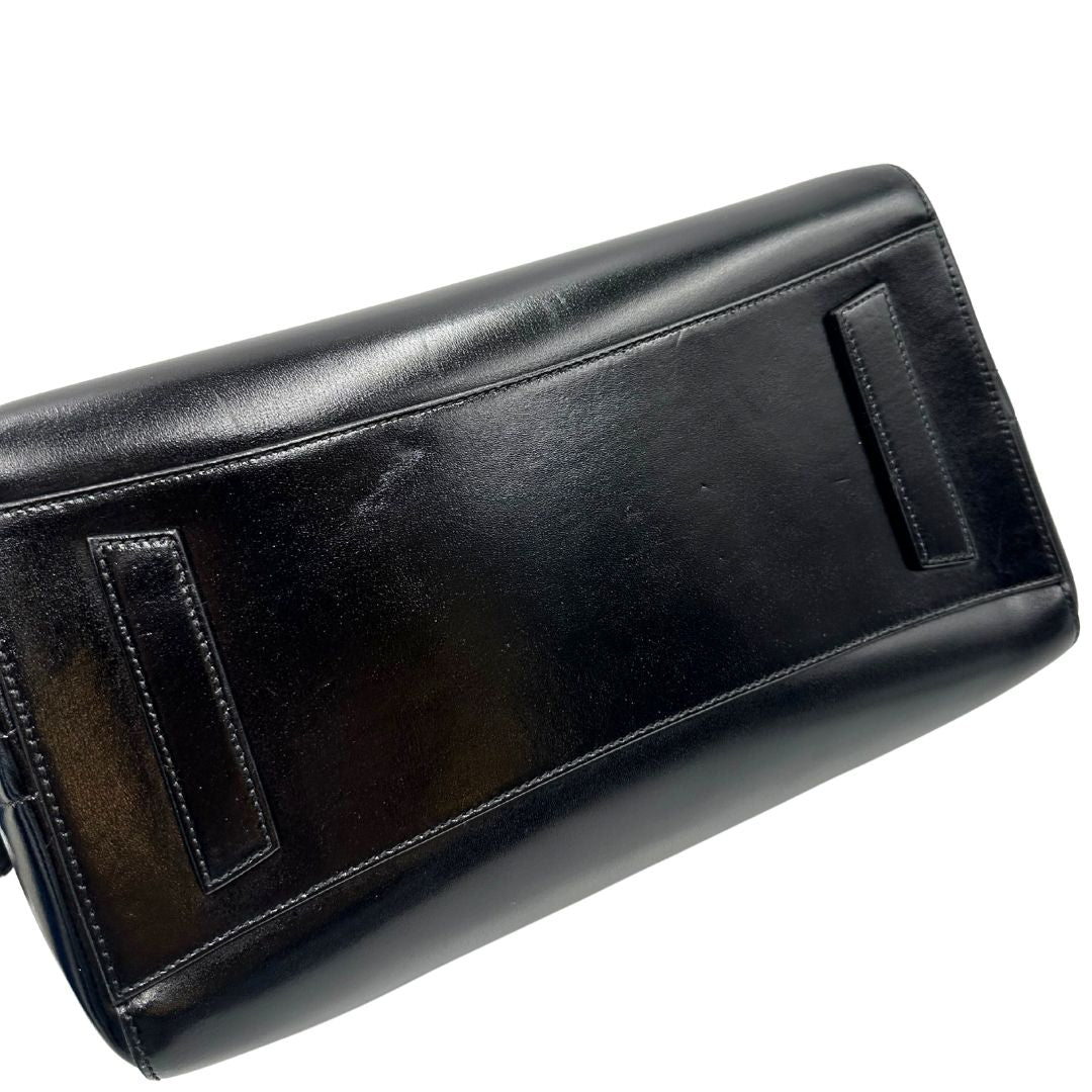 Base di una borsa Givenchy Antigona in pelle nera munita di doppi manici stondati, parti metalliche dorate e una tracolla non amovibile e non regolabile.