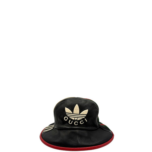 Front di un cappello Gucci x Adidas in pelle nera con logo frontale bianco avorio 'Gucci x Adidas'. Caratterizzato da fascia Web in tessuto verde/rosso e profili rossi.