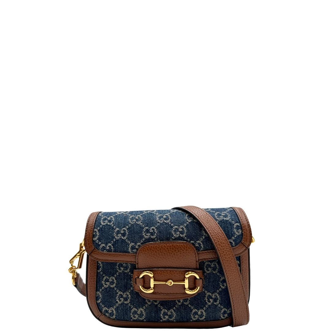 Front di una borsa Gucci in tessuto effetto denim con trama GG , finiture in pelle marroni e parti metalliche dorate; munita di una tracolla Web in tessuto blu e rossa e una tracolla in pelle, entrambe amovibili e regolabili. Completa di dustbag.