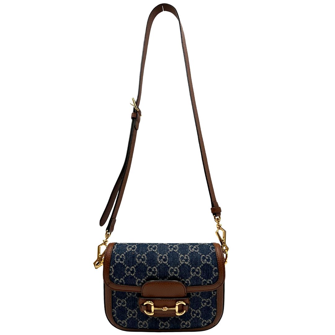 Front di una borsa Gucci in tessuto effetto denim con trama GG , finiture in pelle marroni e parti metalliche dorate; munita di una tracolla Web in tessuto blu e rossa e una tracolla in pelle, entrambe amovibili e regolabili. Completa di dustbag.