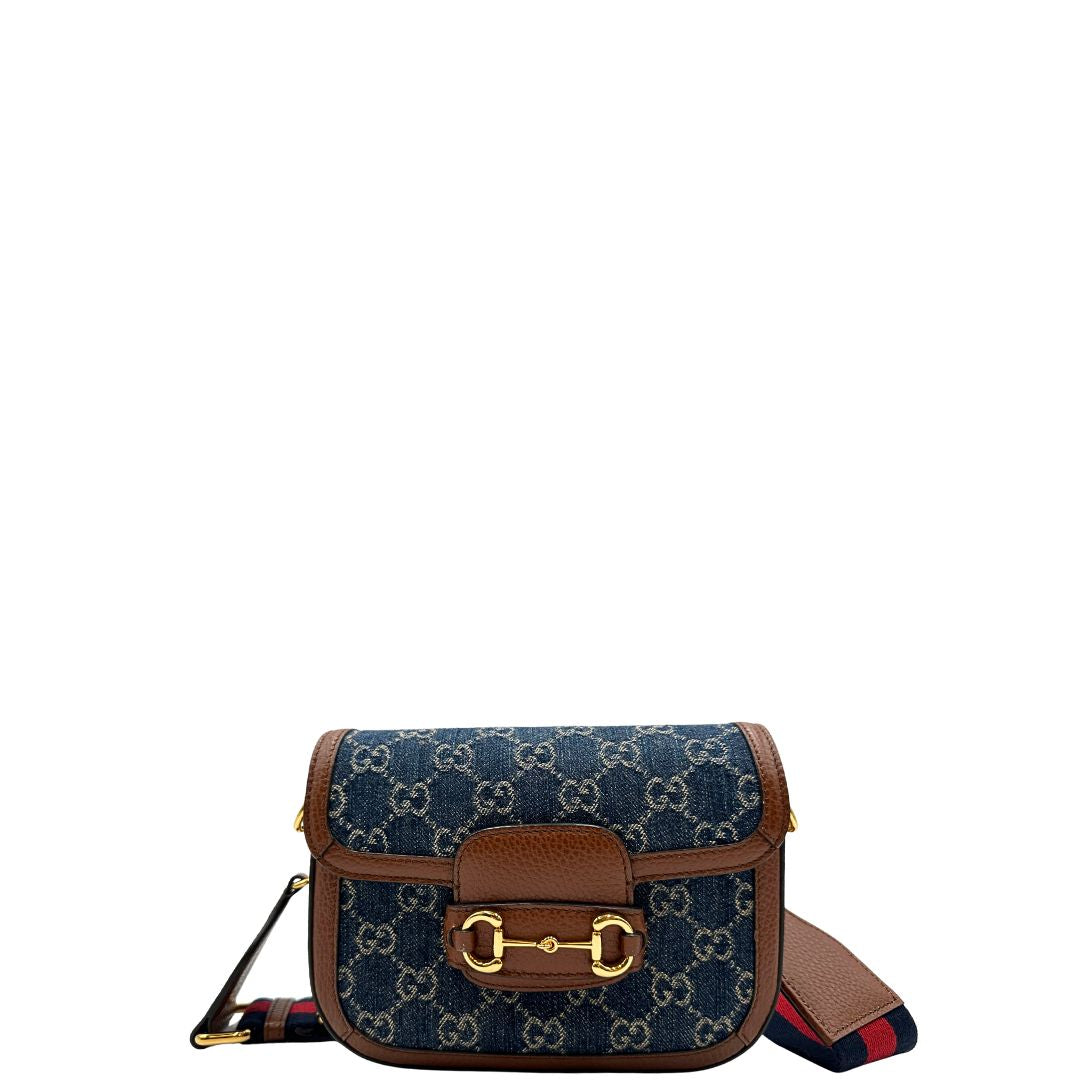 Front di una borsa Gucci in tessuto effetto denim con trama GG , finiture in pelle marroni e parti metalliche dorate; munita di una tracolla Web in tessuto blu e rossa e una tracolla in pelle, entrambe amovibili e regolabili. Completa di dustbag.