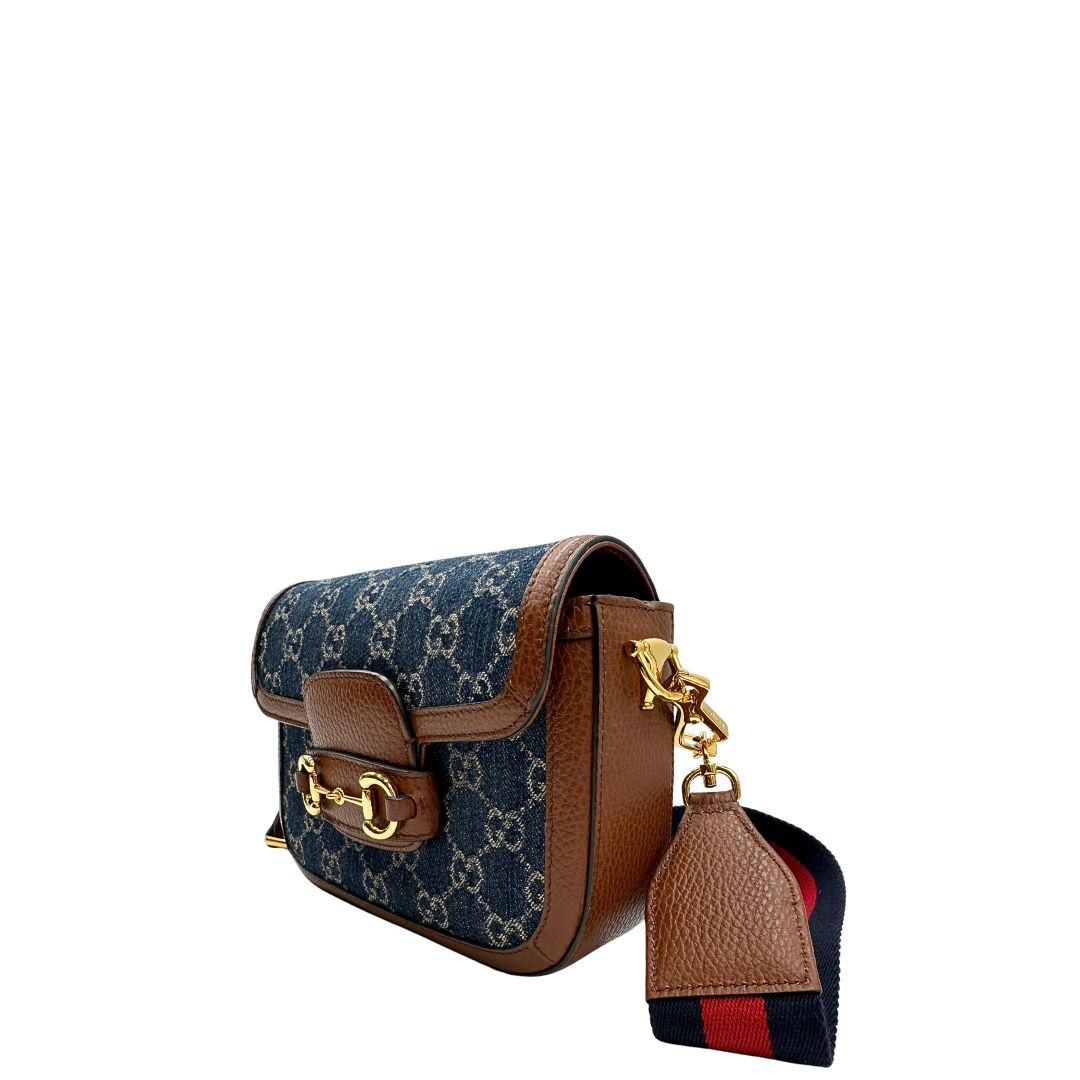 Laterale destro di una borsa Gucci in tessuto effetto denim con trama GG , finiture in pelle marroni e parti metalliche dorate; munita di una tracolla Web in tessuto blu e rossa e una tracolla in pelle, entrambe amovibili e regolabili. Completa di dustbag.