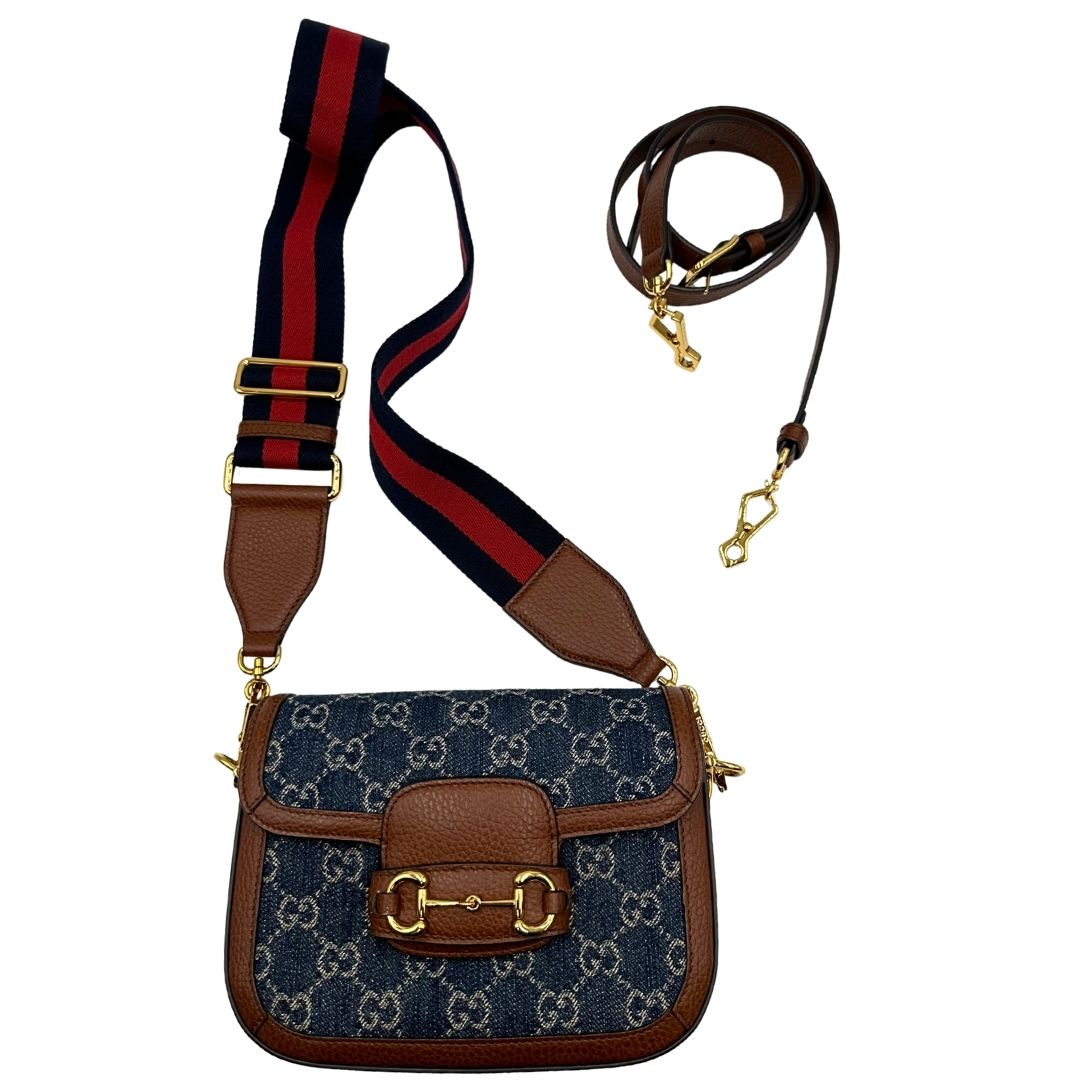 Front di una borsa Gucci in tessuto effetto denim con trama GG , finiture in pelle marroni e parti metalliche dorate; munita di una tracolla Web in tessuto blu e rossa e una tracolla in pelle, entrambe amovibili e regolabili. Completa di dustbag.
