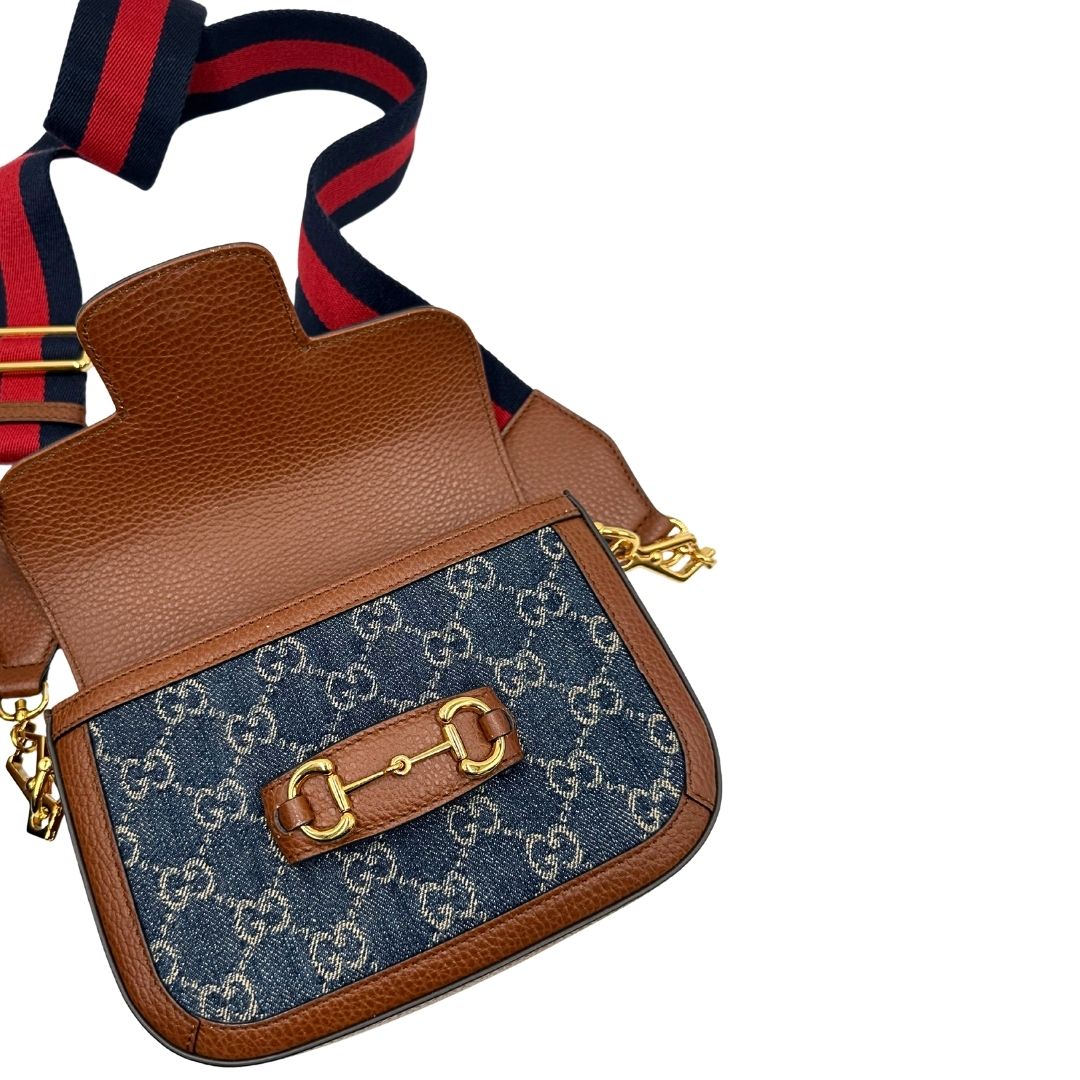 Apertura di una borsa Gucci in tessuto effetto denim con trama GG , finiture in pelle marroni e parti metalliche dorate; munita di una tracolla Web in tessuto blu e rossa e una tracolla in pelle, entrambe amovibili e regolabili. Completa di dustbag.