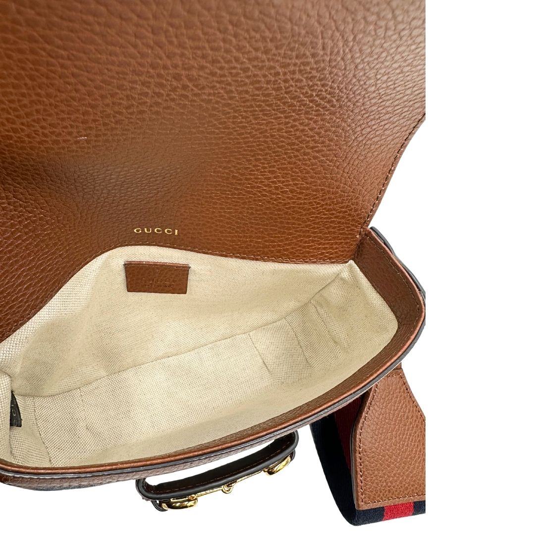 Interno di una borsa Gucci in tessuto effetto denim con trama GG , finiture in pelle marroni e parti metalliche dorate; munita di una tracolla Web in tessuto blu e rossa e una tracolla in pelle, entrambe amovibili e regolabili. Completa di dustbag.