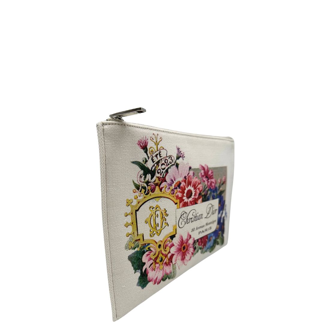 Laterale sinistro di una pochette Dior in tela bianco latte con stampa motivo floreale multicolore e parti metalliche argentate. Munita di dustbag.
