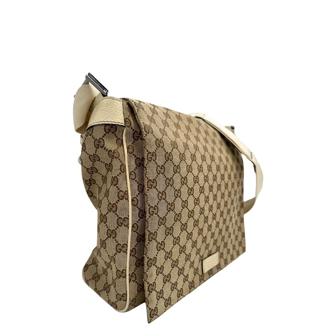 Laterale sinistro di una borsa Gucci in tessuto beige GG , von finiture in pelle bianco avorio con parti metalliche argentate. Munita di tracolla regolabile e non amovibile, in tessuto con spallaccio in pelle. Completa di dustbag. Indossabile a tracolla.