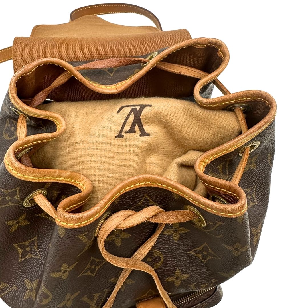 Chiusura di uno zaino Montsouris mini in canvas marrone monogram con finiture in vacchetta naturale e parti metalliche dorate, munito di un anello sulla parte superiore e due bretelle in vacchetta regolabili con fibbie. Completo di dustbag.