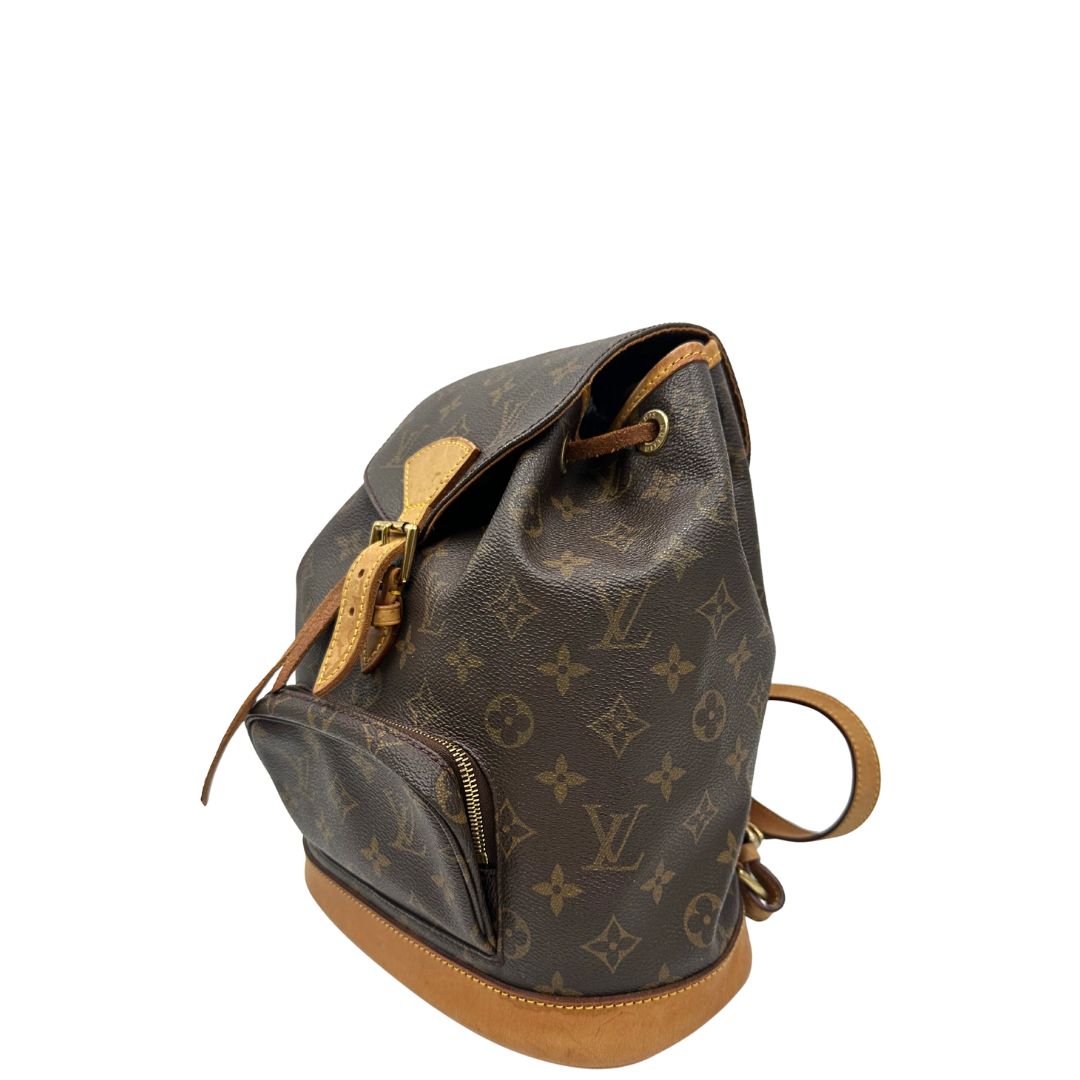 Laterale destro di uno zaino Montsouris mini in canvas marrone monogram con finiture in vacchetta naturale e parti metalliche dorate, munito di un anello sulla parte superiore e due bretelle in vacchetta regolabili con fibbie. Completo di dustbag.