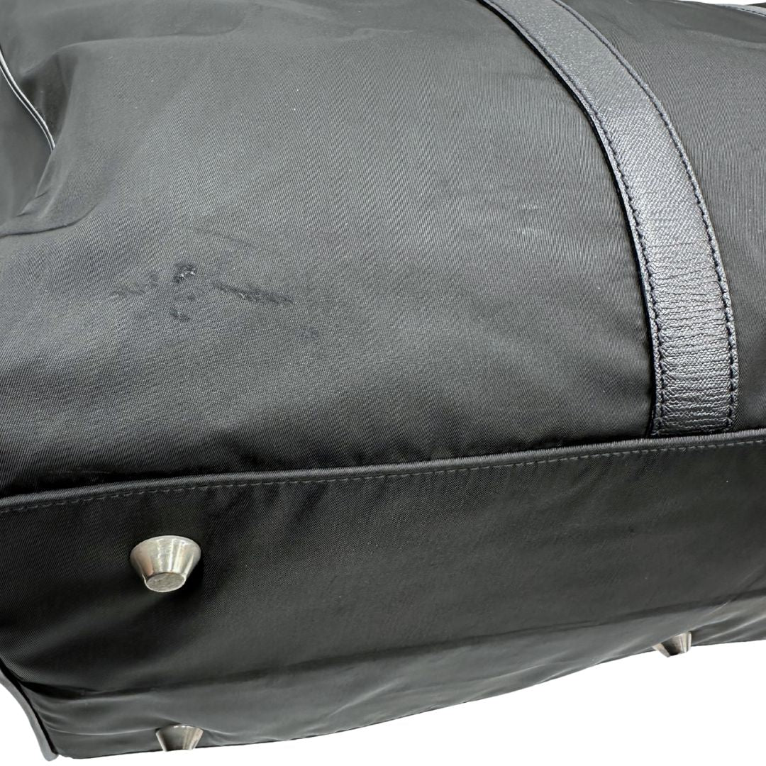 Difetto di un borsone Prada in nylon nero con finiture in pelle Saffiano tono su tono e parti metalliche argentate. Completo di dustbag, tag porta address e lucchetto. Indossabile a mano.