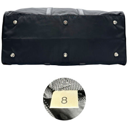 Base e codice di un borsone Prada in nylon nero con finiture in pelle Saffiano tono su tono e parti metalliche argentate. Completo di dustbag, tag porta address e lucchetto. Indossabile a mano.