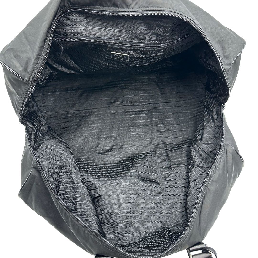 Interno di un borsone Prada in nylon nero con finiture in pelle Saffiano tono su tono e parti metalliche argentate. Completo di dustbag, tag porta address e lucchetto. Indossabile a mano.